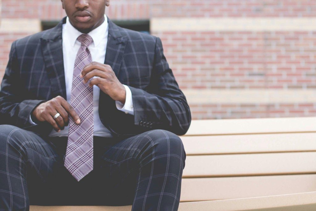 A confident, professional man adjusts his tie while sitting outdoors, showcasing style and poise.